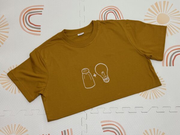 Salt & Light Tees embroidered in cream thread as a line art of salt and light icons. Shirt color is in mustard.